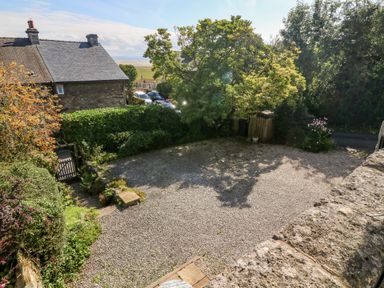 A gravel driveway surrounded by trees and bushes near a stone house at Westmorland Cottage in Grange-Over-Sands