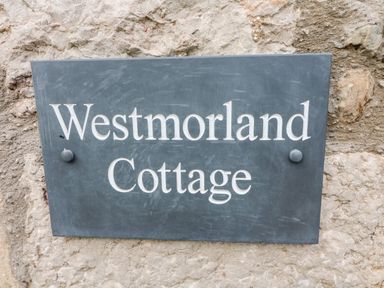 A rectangular dark plaque with white text Westmorland Cottage fixed on a stone wall