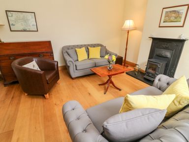 A sitting room with gray sofas yellow cushions a brown leather chair a wooden table and a fireplace at Westmorland Cottage in Grange-Over-Sands