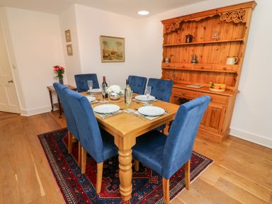 A dining room with a wooden table set for six with blue chairs and a wooden cabinet against the wall at Westmorland Cottage in Grange-Over-Sands