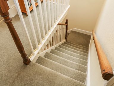 A carpeted staircase with wooden handrails and white balusters at Westmorland Cottage in Grange-Over-Sands