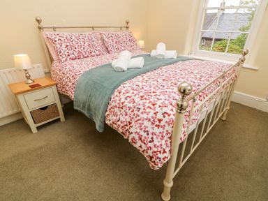 A bedroom with a bed with floral bedding and a nightstand with a lamp at Westmorland Cottage in Grange-Over-Sands