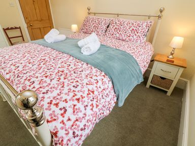 A bedroom with a bed with floral bedding and rolled towels on top a bedside table with a lamp and a wooden door at Westmorland Cottage in Grange-Over-Sands