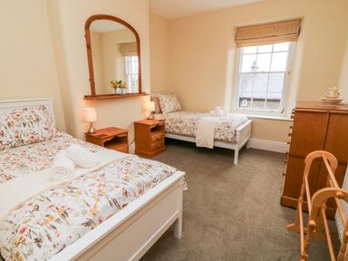 A bedroom with two single beds a wooden dresser and a wooden clothes rack at Westmorland Cottage in Grange-Over-Sands