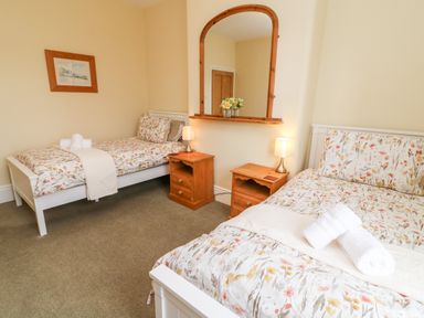 A bedroom with two single beds floral bedding bedside tables lamps and a mirror at Westmorland Cottage in Grange-Over-Sands