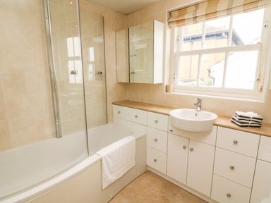 A bathroom with a bathtub shower combination sink with cabinet and window at Westmorland Cottage in Grange-Over-Sands