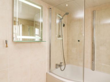 A bathroom with a bathtub shower combination glass shower screen and a lighted mirror at Westmorland Cottage in Grange-Over-Sands