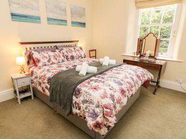 A bedroom with a double bed with floral bedding and rolled towels on a grey throw at Westmorland Cottage in Grange-Over-Sands