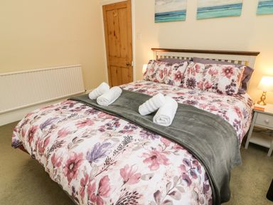 A bedroom with a bed with floral bedding and rolled towels at Westmorland Cottage in Grange-Over-Sands