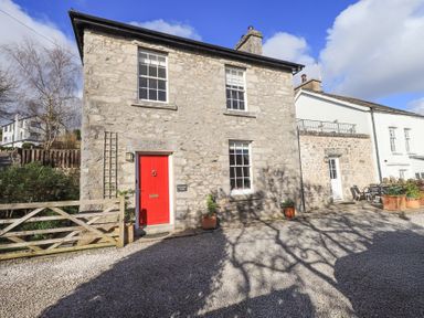 A stone cottage with a red door and wooden gate with pots outside at Westmorland Cottage in Grange-Over-Sands