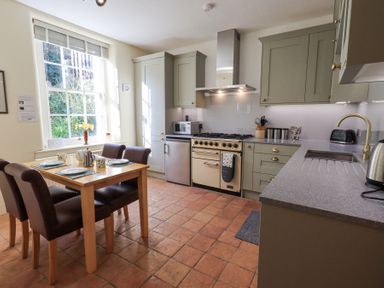 A kitchen with a wooden dining table and four chairs a stove oven a microwave and a sink at Westmorland Cottage in Grange-Over-Sands