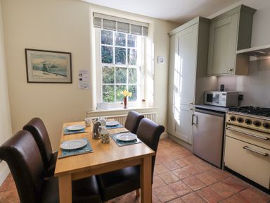 A kitchen with a wooden dining table set for four and cabinets with appliances at Westmorland Cottage in Grange-Over-Sands