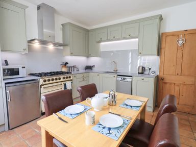 A kitchen with a wooden table set for four with plates and a teapot at Westmorland Cottage in Grange-Over-Sands