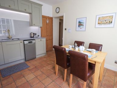 A kitchen with a dining table set for four and kitchen cabinets with a sink at Westmorland Cottage in Grange-Over-Sands