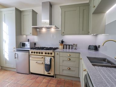 A kitchen with green cabinets a stove a microwave a toaster and a sink at Westmorland Cottage in Grange-Over-Sands