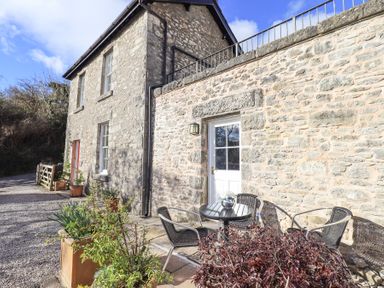 Exterior view of a stone cottage with a small patio table and chairs outside a white door at Westmorland Cottage in Grange-Over-Sands
