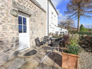 An outdoor patio area with a round table and four chairs next to a stone wall and a door at Westmorland Cottage in Grange-Over-Sands