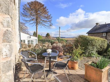 An outdoor patio with a round table and four chairs surrounded by plants and stone walls at Westmorland Cottage in Grange-Over-Sands