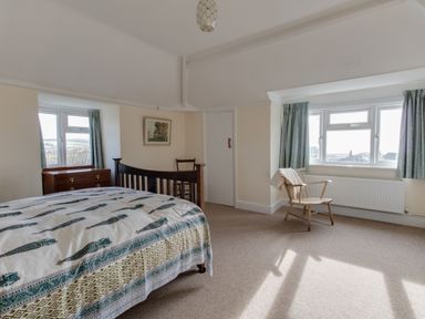 A bedroom with a bed a wooden chair a chest of drawers and windows with curtains at Thorncroft in West Bay