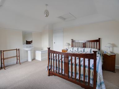 A bedroom with a wooden bed, two bedside tables with lamps, a sink with a mirror, and a wooden towel rack at Thorncroft in West Bay