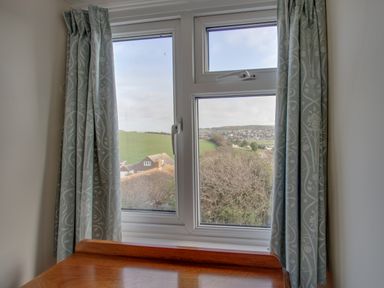 A window with patterned curtains and a wooden table below showing a countryside view at Thorncroft in West Bay