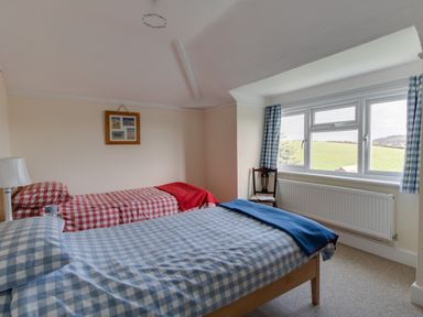 A bedroom with two single beds covered with checkered bedding near a window with blue checkered curtains at Thorncroft in West Bay