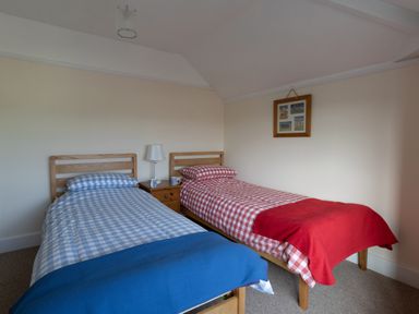 A bedroom with two single beds with checkered bedding and a small wooden nightstand with a lamp at Thorncroft in West Bay