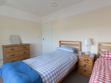 A bedroom with two single beds a wooden dresser and a nightstand with a lamp at Thorncroft in West Bay
