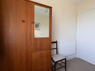 A wooden wardrobe with a mirror a wooden chair with a cushioned seat a white radiator and a closed white door in a small room at Thorncroft in West Bay