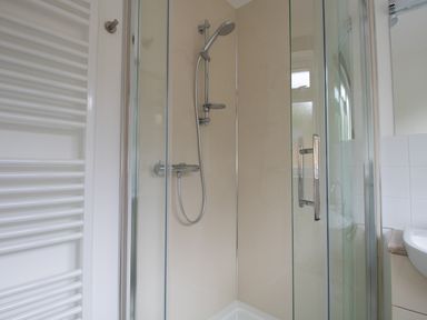 A bathroom shower with glass doors a wall-mounted showerhead and a towel radiator at Thorncroft in West Bay