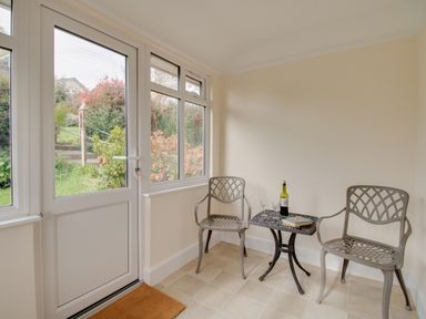 A small sunroom with two metal chairs and a table holding a bottle and book at Thorncroft in West Bay