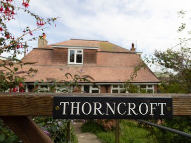 A wooden gate with a Thorncroft sign and a house with a tiled roof in the background at Thorncroft in West Bay
