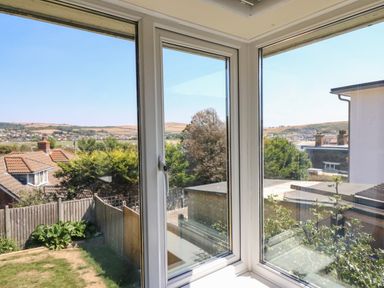 A view of rooftops trees and hills through corner windows at Thorncroft in West Bay