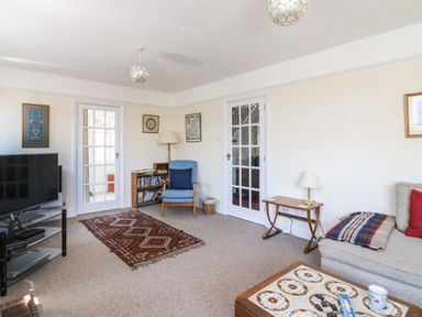A living room with a television a blue chair a wooden bookshelf and a sofa at Thorncroft in West Bay