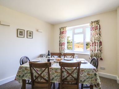 A dining room with a table set for six near a window with floral curtains at Thorncroft in West Bay