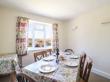 A dining room with a table set with plates glasses and a bottle with floral tablecloths and floral curtains at Thorncroft in West Bay