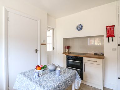 A kitchen with a table covered by a tablecloth and fruit bowl a teapot and cups next to a stove and oven at Thorncroft in West Bay