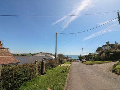 A street with houses cars and grass with a view of the sea at Thorncroft in West Bay