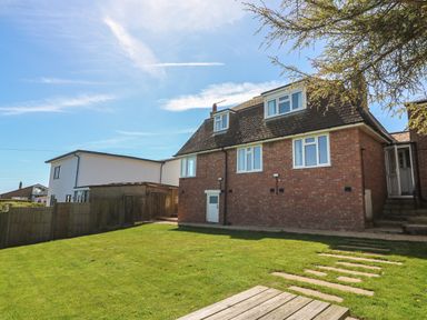 A backyard with a lawn and a brick house with multiple windows and a wooden fence at Thorncroft in West Bay