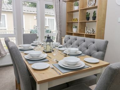 A dining room with a wooden table set for six with grey chairs and a wooden shelf with decor at Cayton Pines Cayton Bay near Scarborough