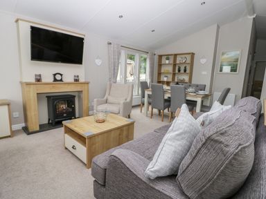 A living room with a gray sofa and cushions a wooden coffee table an armchair and a dining table with chairs at Cayton Pines in Cayton Bay near Scarborough