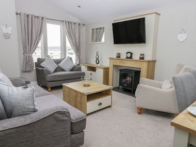 A living room with sofas a wooden coffee table a wall-mounted TV and a fireplace at Cayton Pines in Cayton Bay near Scarborough