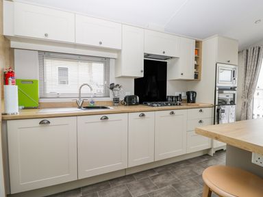 A kitchen with white cabinets a sink a gas stove an oven a microwave and kitchen utensils at Cayton Pines Cayton Bay near Scarborough