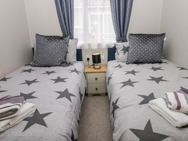 A bedroom with two single beds with star patterned bedding and a small bedside table with a lamp at Cayton Pines Cayton Bay near Scarborough