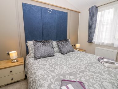 A bedroom with a double bed with decorative pillows bedside tables with lamps and a window with curtains at Cayton Pines in Cayton Bay near Scarborough