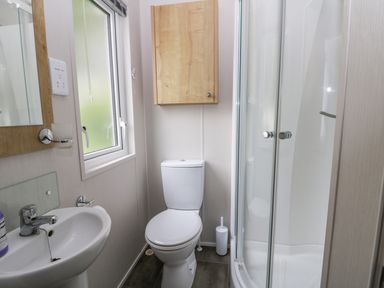 A small bathroom with a sink, toilet, wall cabinet, window, and shower at Cayton Pines in Cayton Bay near Scarborough