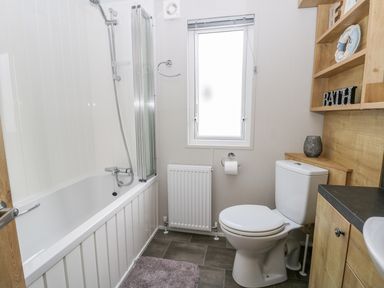 A bathroom with a bathtub shower combination a toilet a wooden cabinet and shelves a window and a radiator at Cayton Pines Cayton Bay near Scarborough