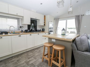 A kitchen with white cabinets a wooden countertop two wooden stools a gray sofa and sliding glass doors at Cayton Pines in Cayton Bay near Scarborough