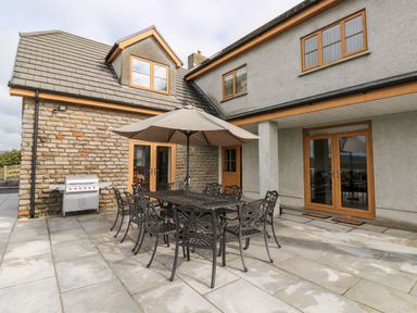 An outdoor patio with a metal dining table and chairs under a large umbrella next to a barbecue grill at Grooms Quarters at Pant y Gaseg Farm in Ammanford