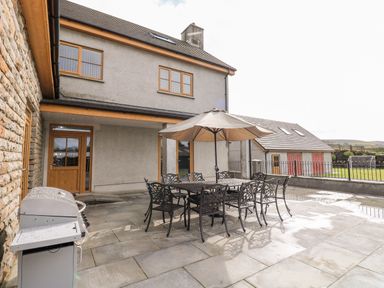 An outdoor patio area with a metal dining table and chairs under an umbrella next to a barbecue grill at Grooms Quarters at Pant y Gaseg Farm in Ammanford